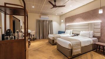 A hotel room with two beds, a ceiling fan, an air conditioning unit, a wooden desk with a mirror, and a patterned wall.
