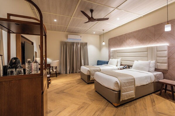 Une chambre d’hôtel avec deux lits, un ventilateur de plafond, un appareil de climatisation, un bureau en bois avec un miroir et un mur décoré de motifs.