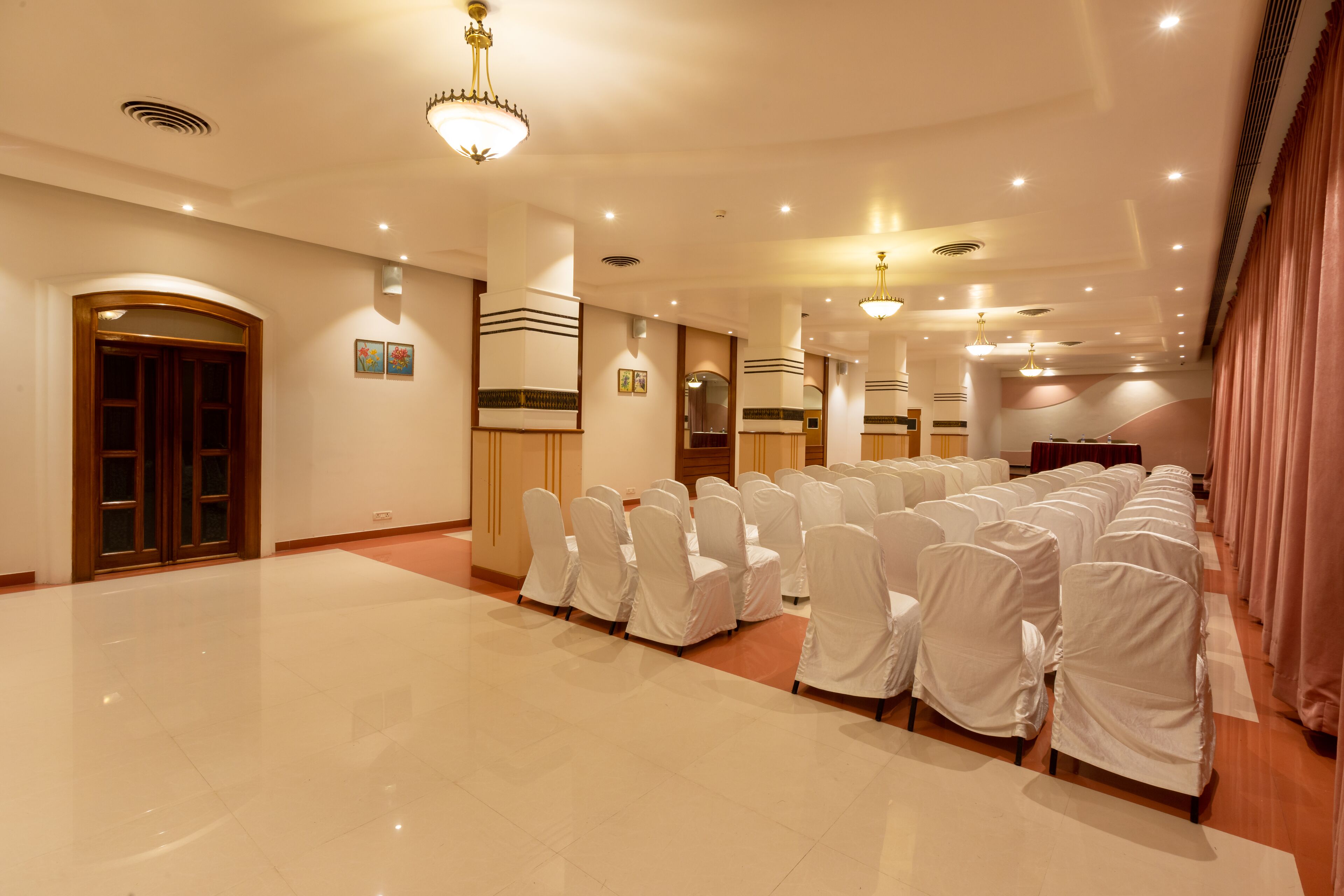 A spacious hall with rows of chairs covered in white, a wooden door, and a stage area.