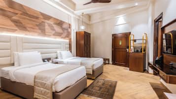 Habitación de hotel con dos camas, ventilador de techo, cabecera de madera, armario, escritorio con espejo y cafetera.