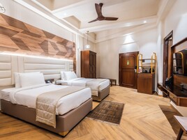 Habitación de hotel con dos camas, ventilador de techo, cabecera de madera, armario, escritorio con espejo y cafetera.