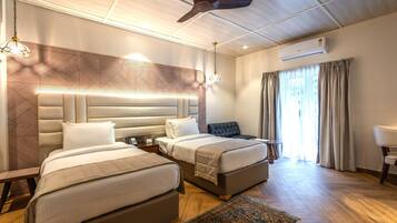 Ein Hotelzimmer mit zwei Betten, einem Deckenventilator, einer Klimaanlage, einem Fenster mit Vorhängen und einem gemusterten Teppich.