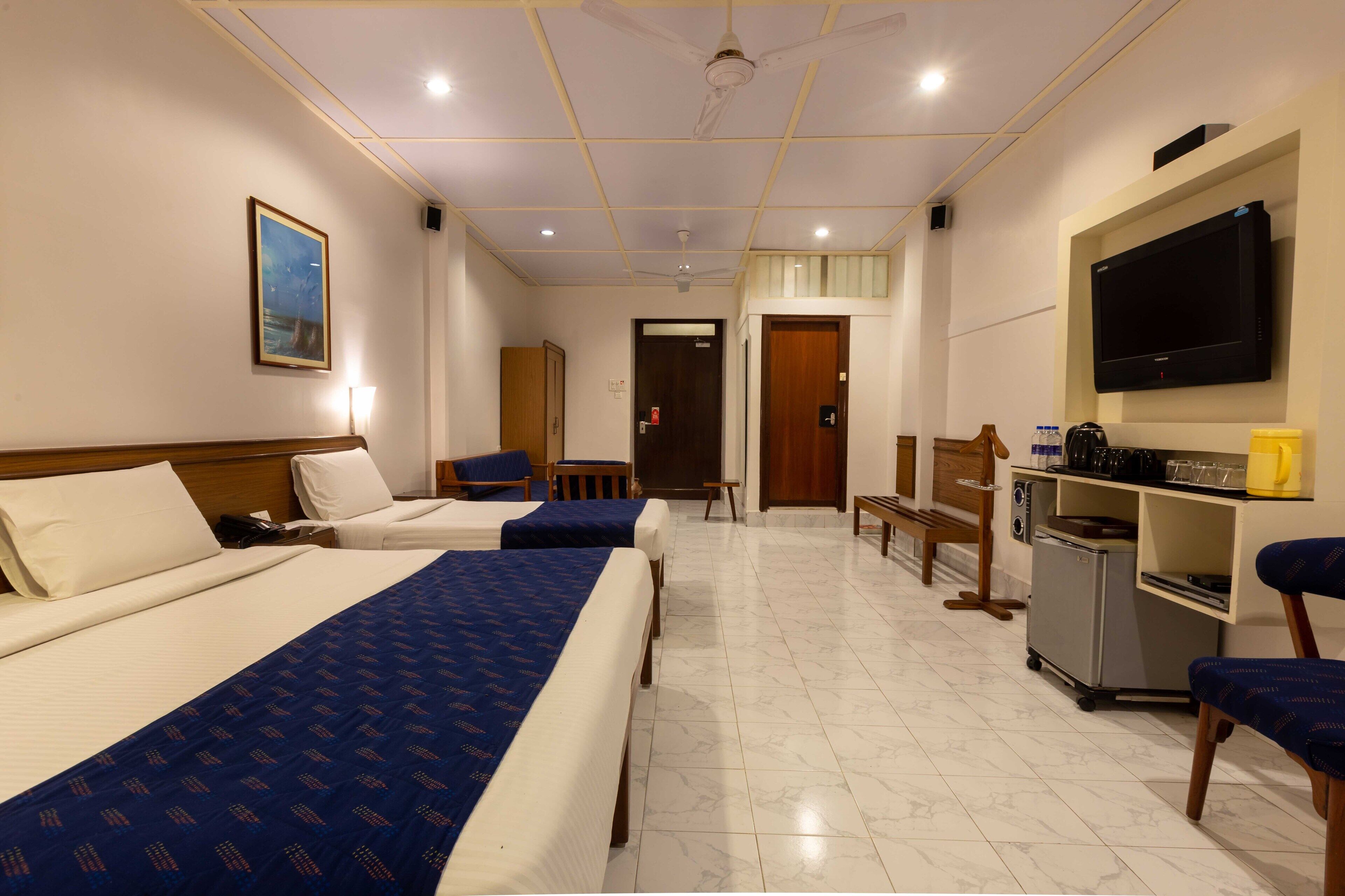Une chambre d’hôtel avec deux lits, une télévision, une kitchenette et une porte donnant sur une autre chambre.
