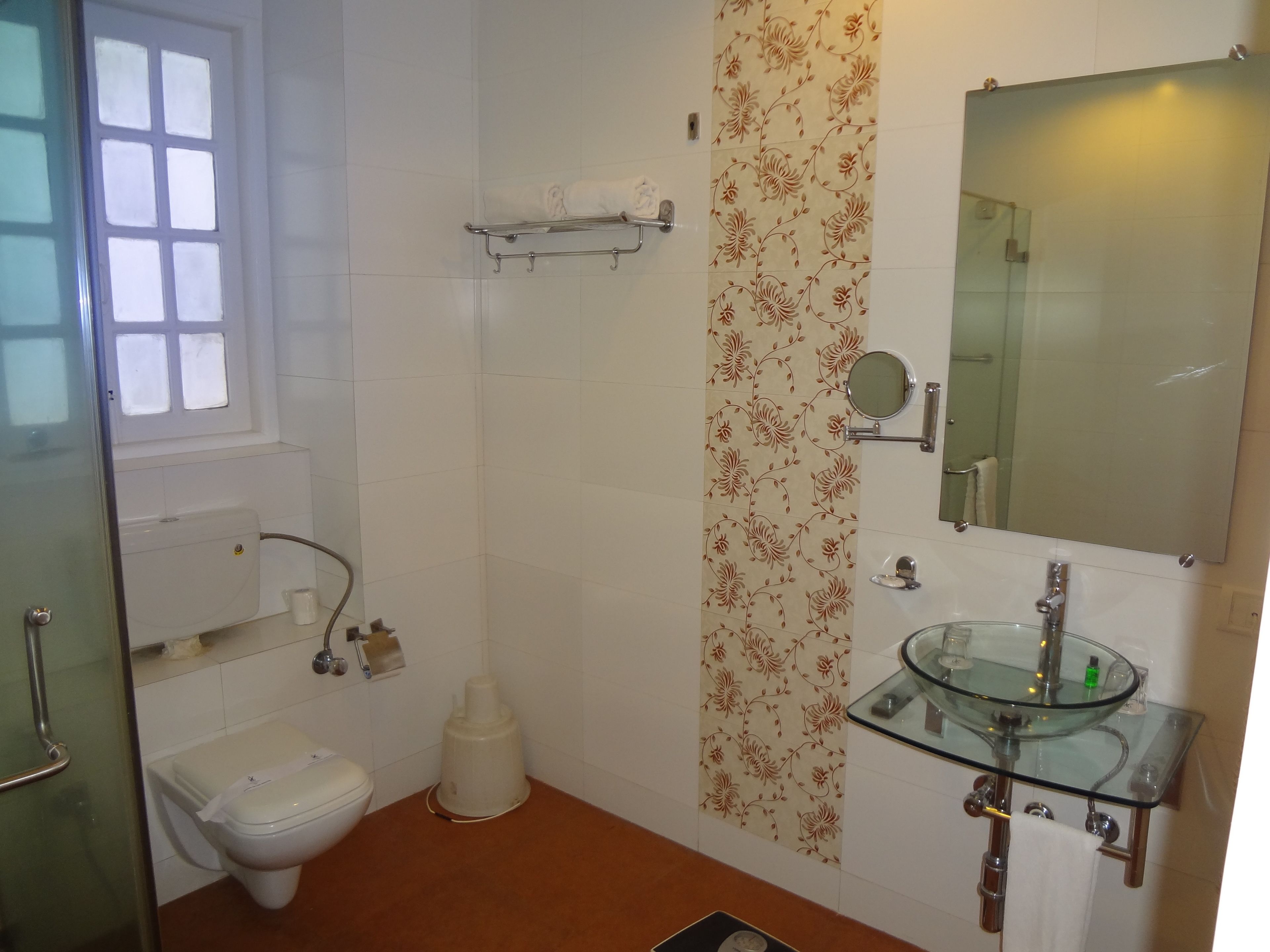 A bathroom with a toilet, sink, shower, and a glass-topped vanity.