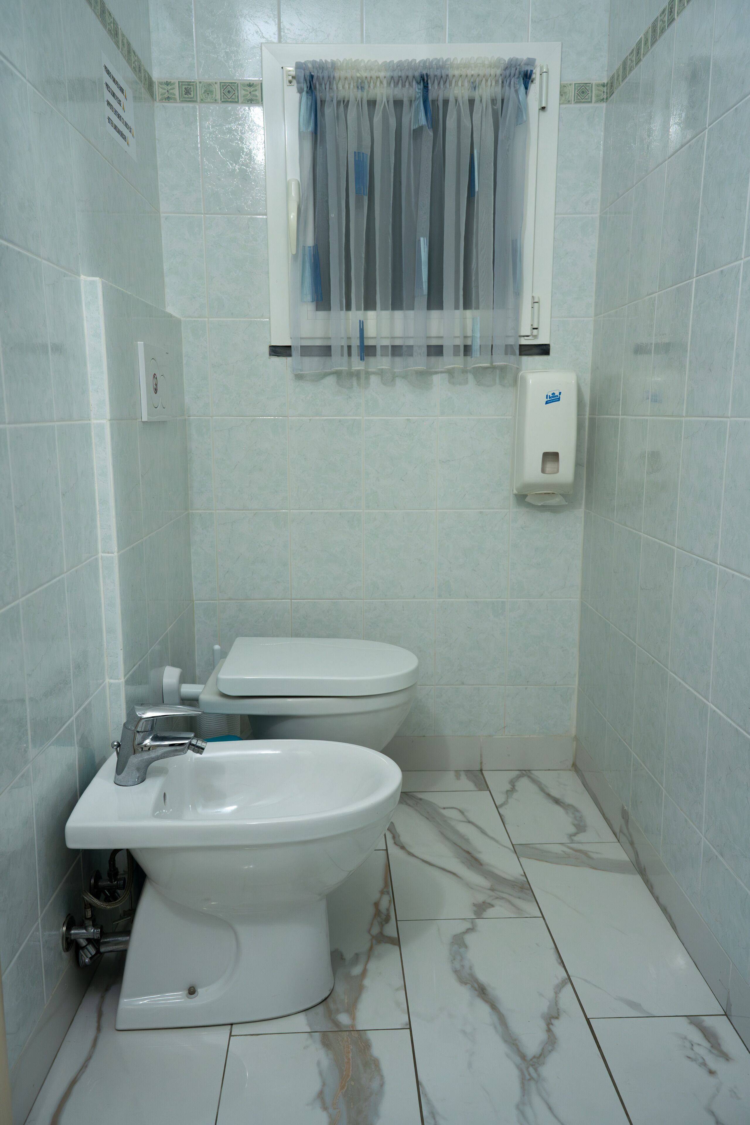 Baño con inodoro, bidé y dispensador de jabón para manos.