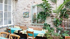 En udendørs patio med stenvægge, træborde og stole.