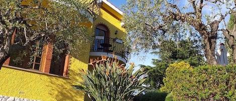 Un edificio amarillo con balcón, rodeado de jardines y árboles cuidados.