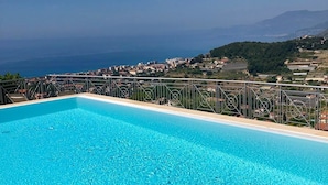 A rectangular swimming pool with clear blue water, surrounded by a metal railing. In the background, there is a view of a coastal town with buildings and greenery. - La Finestra sul Mare (Bordighera)
