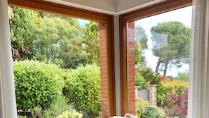 A corner seating area with a white sofa, two brown cushions, and a view of a garden through large windows. - La Finestra sul Mare (Bordighera)