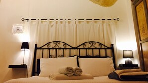 A hotel room with a stone archway, a bed with white linens, two bedside lamps, and a wooden cabinet.