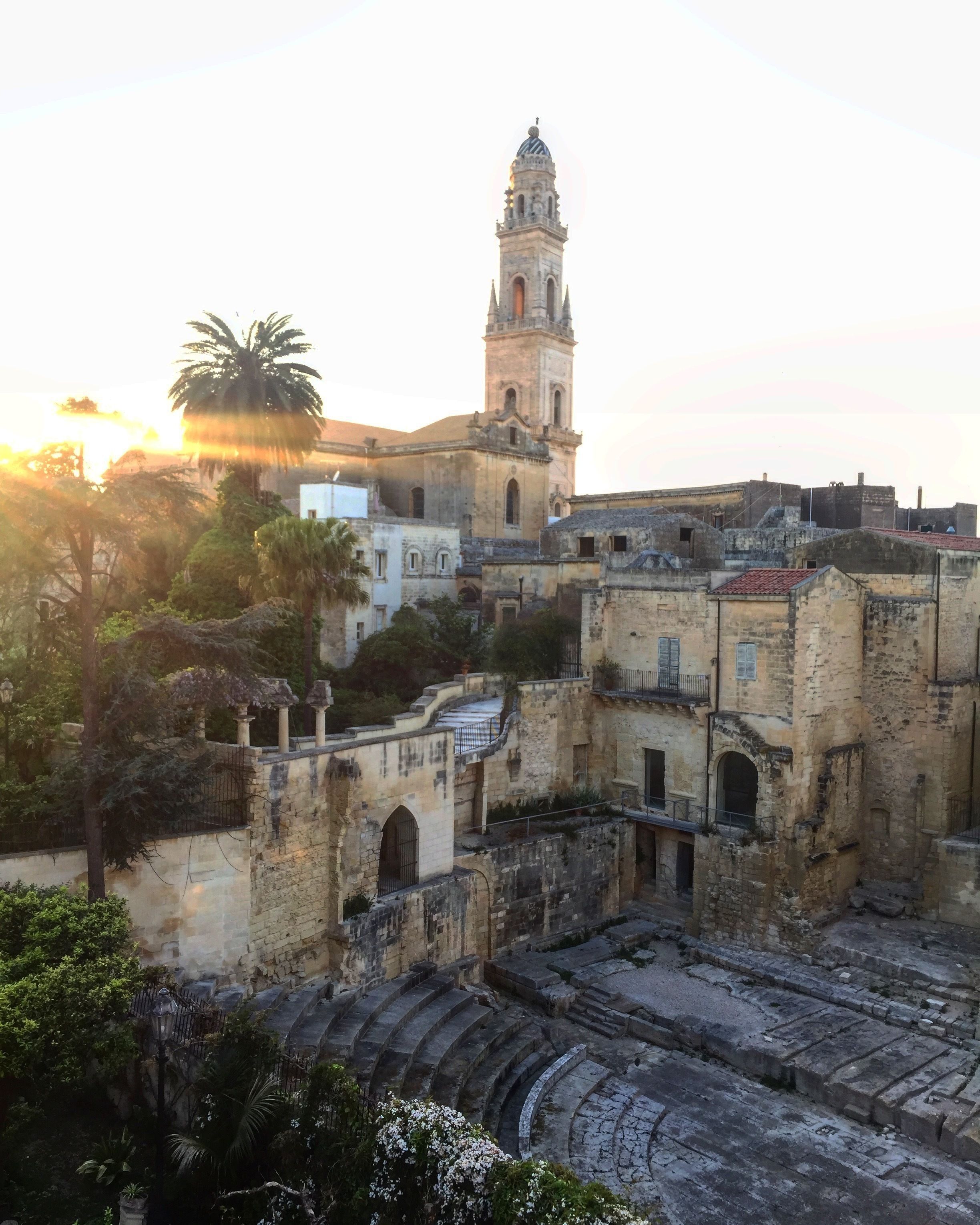 An ancient cityscape with a prominent tower and ruins, including an amphitheater.