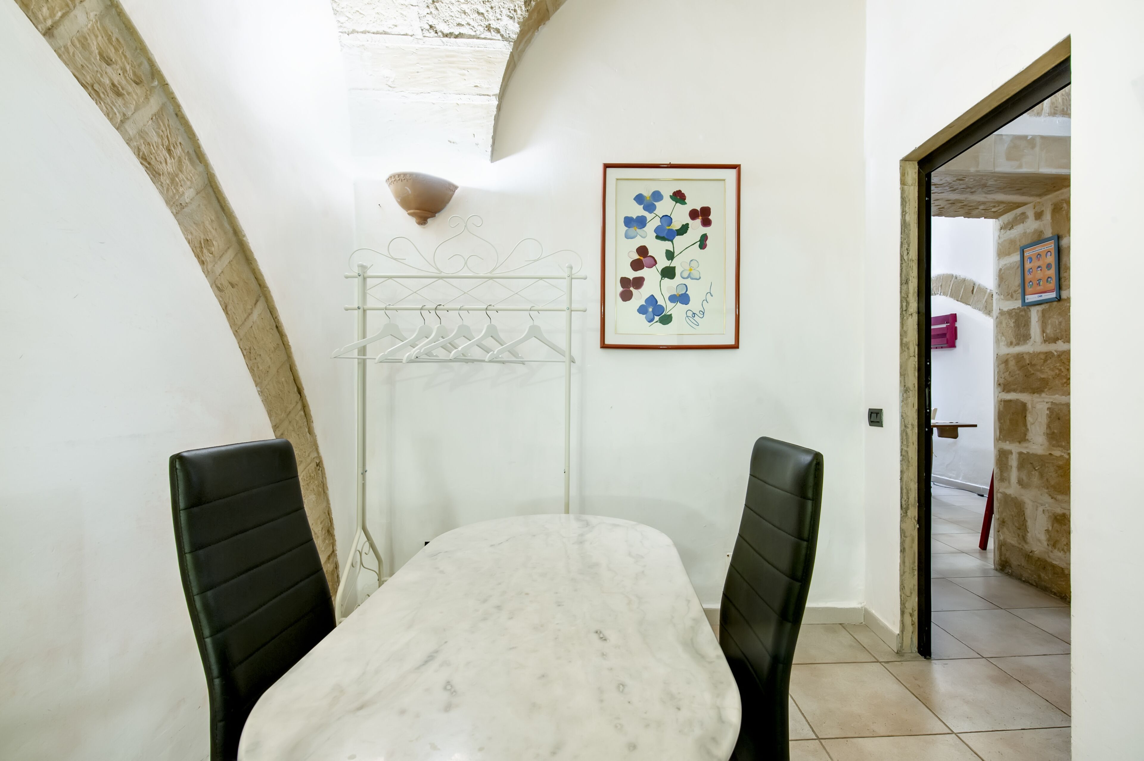 A dining area with a marble table and black chairs, a wall-mounted light fixture, and a framed floral artwork.