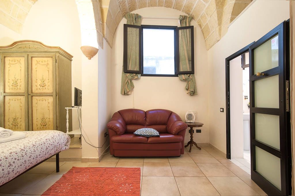 Une chambre à coucher avec un lit, un canapé en cuir rouge, une petite table et une fenêtre avec des rideaux.