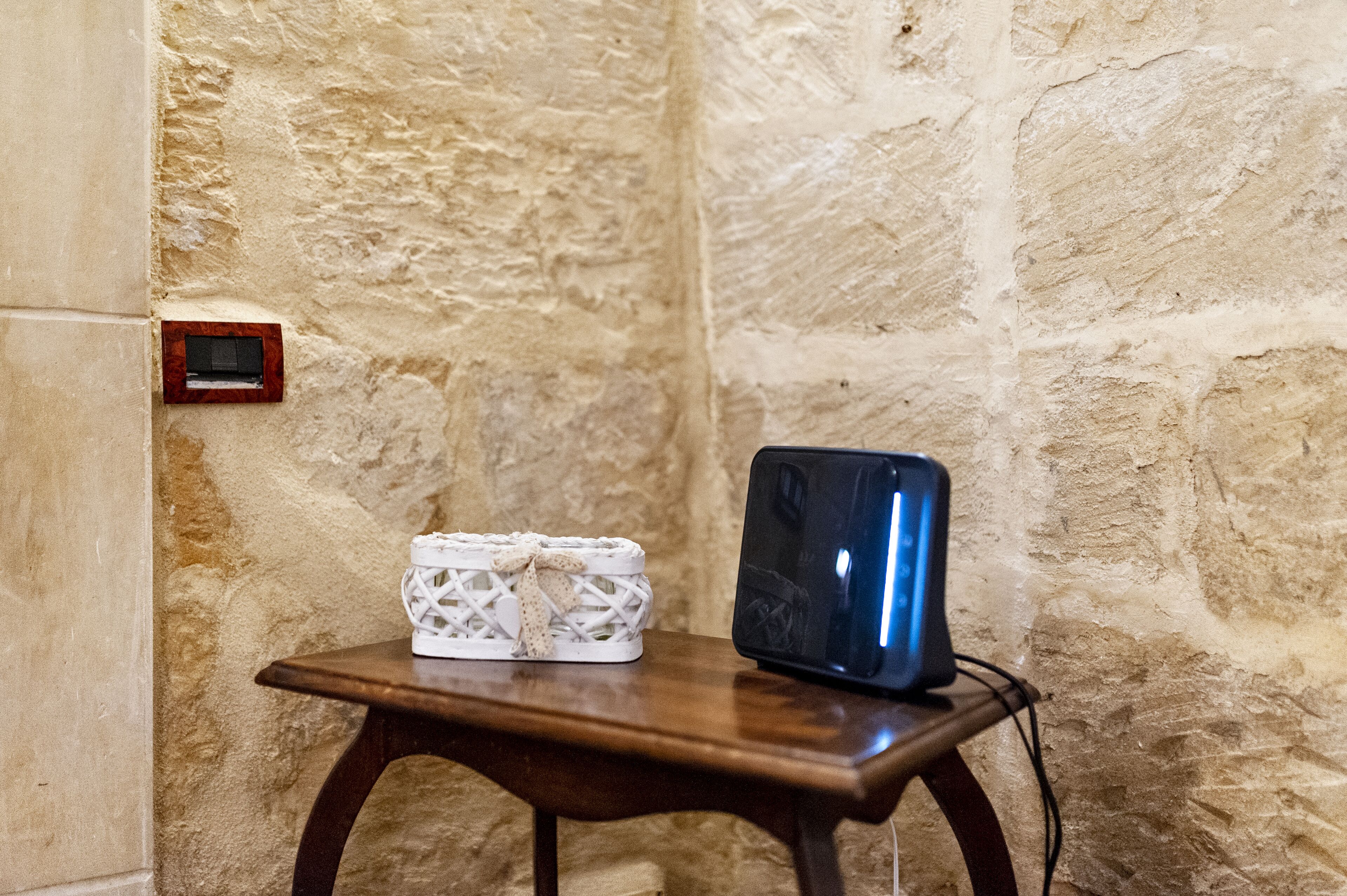 A wooden table with a white woven basket and a black tablet on it, against a textured stone wall.