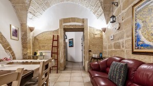 A stone-walled room with a wooden dining table, a red leather sofa, and a staircase leading to another room.