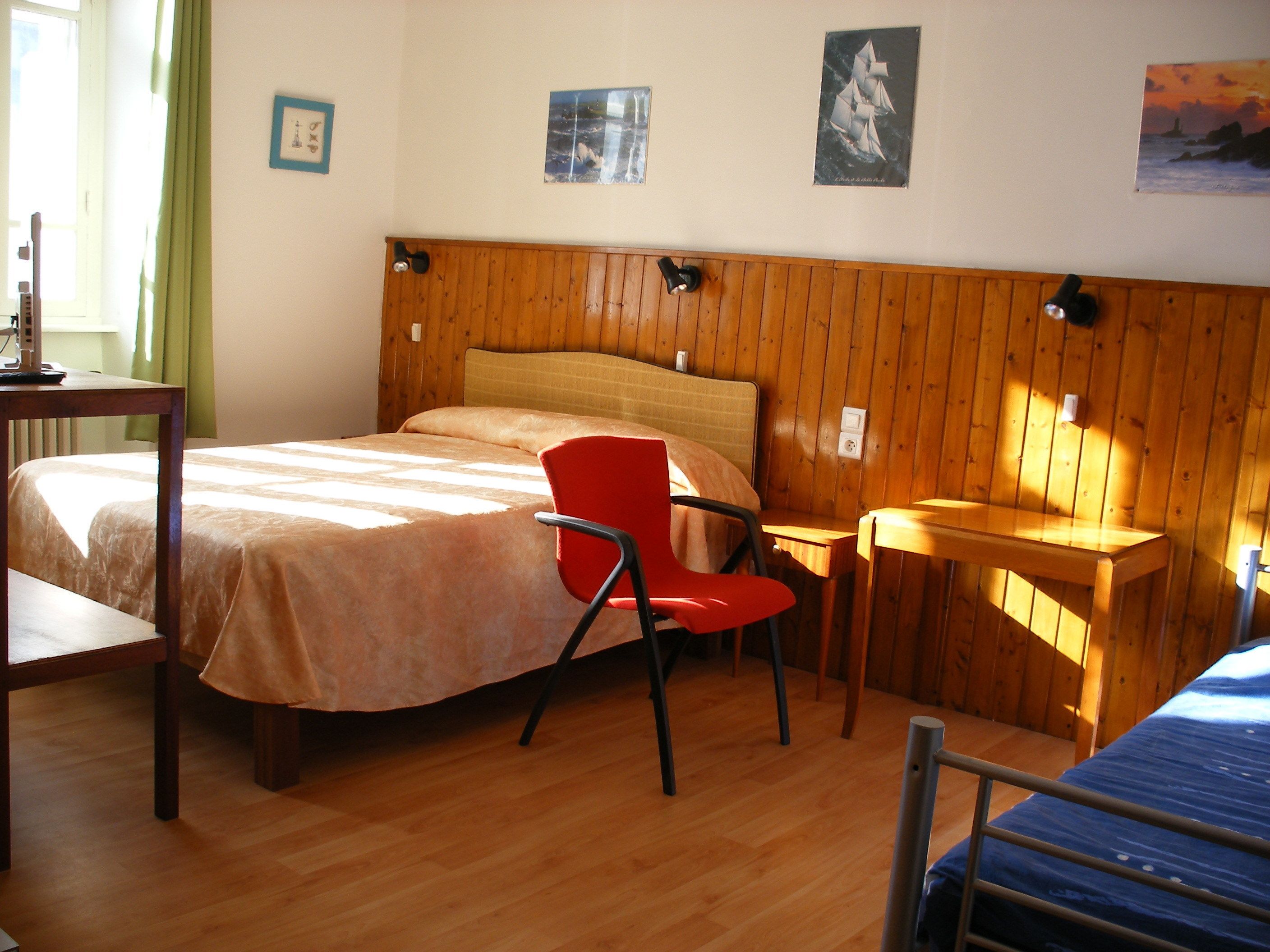 A room with a bed, a red chair, a small table, and wooden walls.