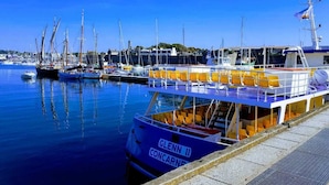 Uma marina com barcos atracados, incluindo um barco azul chamado "GLENN II" com bancos amarelos e uma cabine branca.