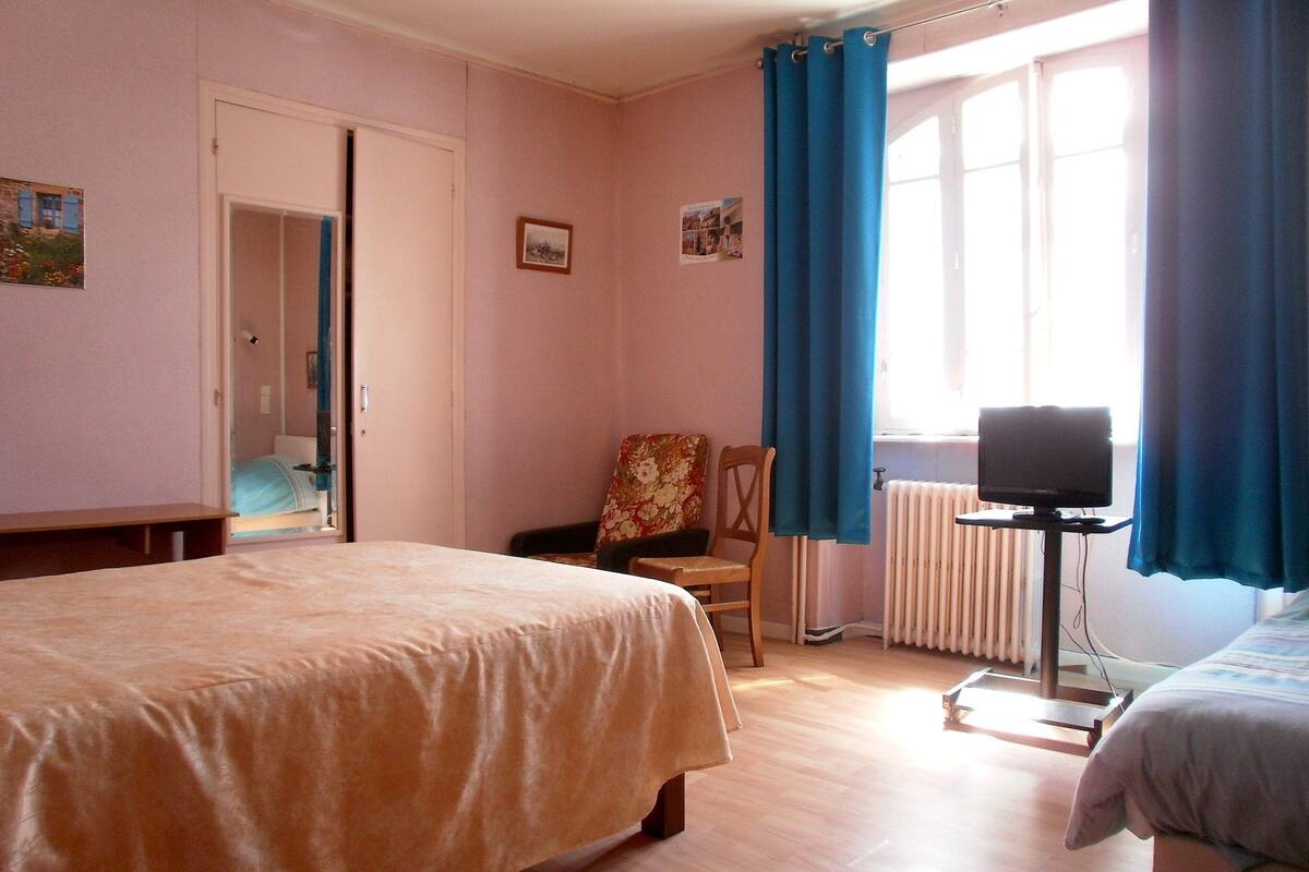 A bedroom with a bed, a chair, a desk, a television, and a window with curtains.