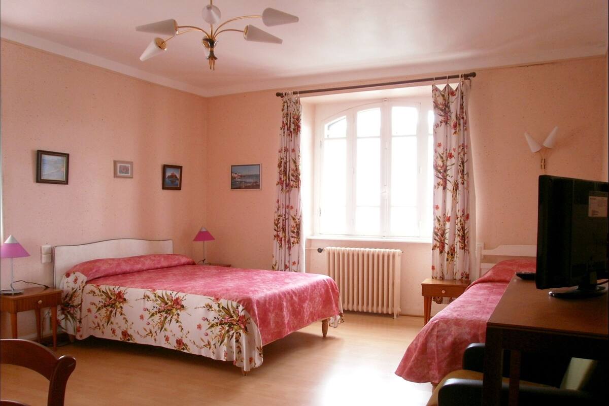 A bedroom with a bed, a desk, a chair, a radiator, a ceiling fan, and a window with curtains.