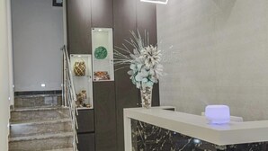 Un área de recepción moderna con mostrador de mármol, un florero con flores decorativas y una escalera que conduce a una puerta con un adorno circular verde.