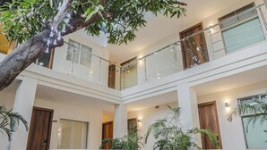 Un vestíbulo de hotel de varios niveles con una escalera central, barandales de vidrio y plantas de interior.