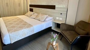 Un dormitorio moderno con una cama grande, ventilador de techo, luz empotrada en la pared y una pequeña mesa con un florero.