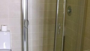 Een badkamer met een douchecabine van glas, een toilet en een papieren handdoekdispenser.