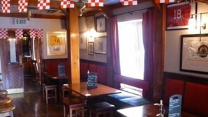 Een restaurantinterieur met houten tafels, rood-wit geruit lopers, ingelijste foto’s aan de wanden en een bord met de tekst ‘uitgang’.