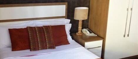 Une chambre d’hôtel comprenant un lit, une table de chevet avec une lampe, un téléphone et une armoire.