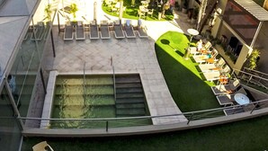 Un área de piscina en la azotea con sillones de descanso, una pequeña mesa y una sección con césped.