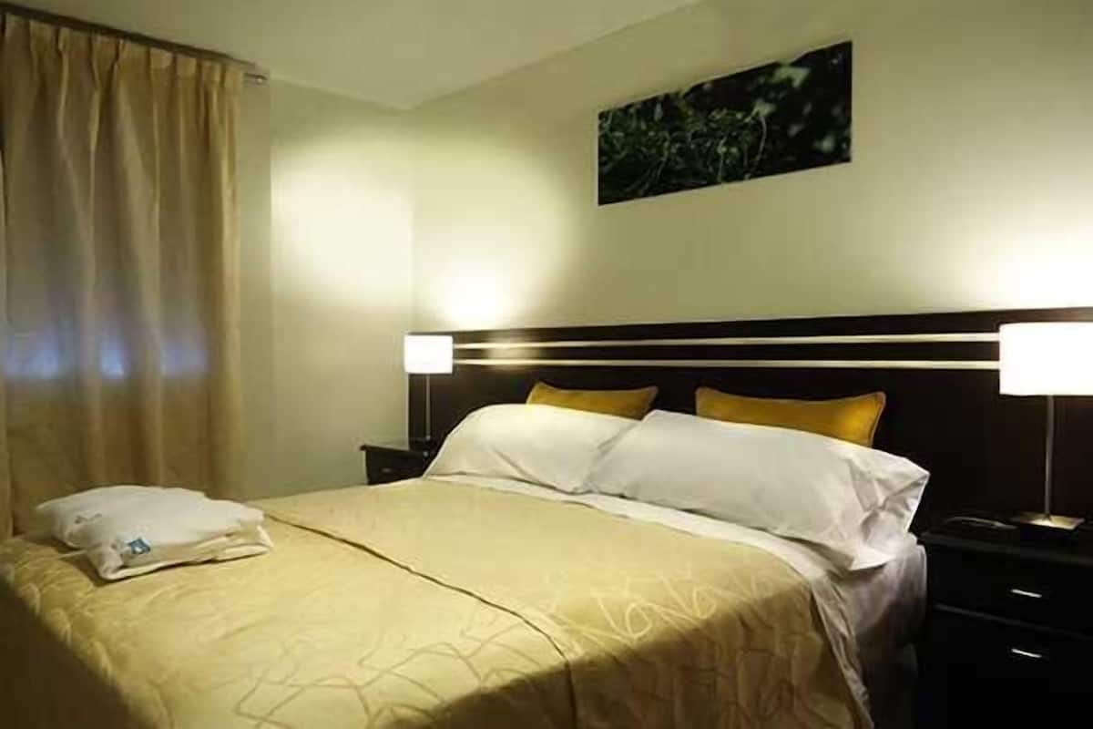 A hotel room with a neatly made bed, a bedside table with a lamp, and a painting on the wall.