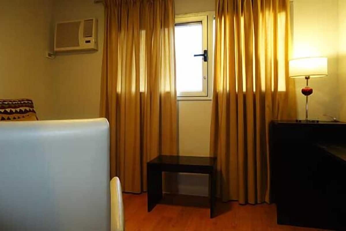 A hotel room with a bed, a small table, a desk, a lamp, and curtains.