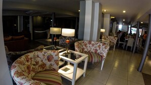 Un hall de hotel con un sofá, sillones, una mesa de centro y una zona de comedor.