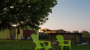 Un patio trasero con dos sillas verde brillante, una mesita y una hamaca bajo un árbol grande.