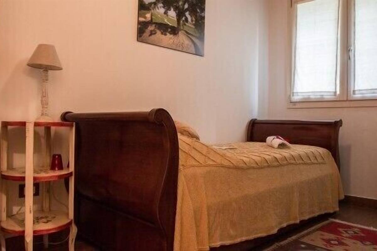 A bedroom with a single bed, a nightstand, a lamp, and a window.