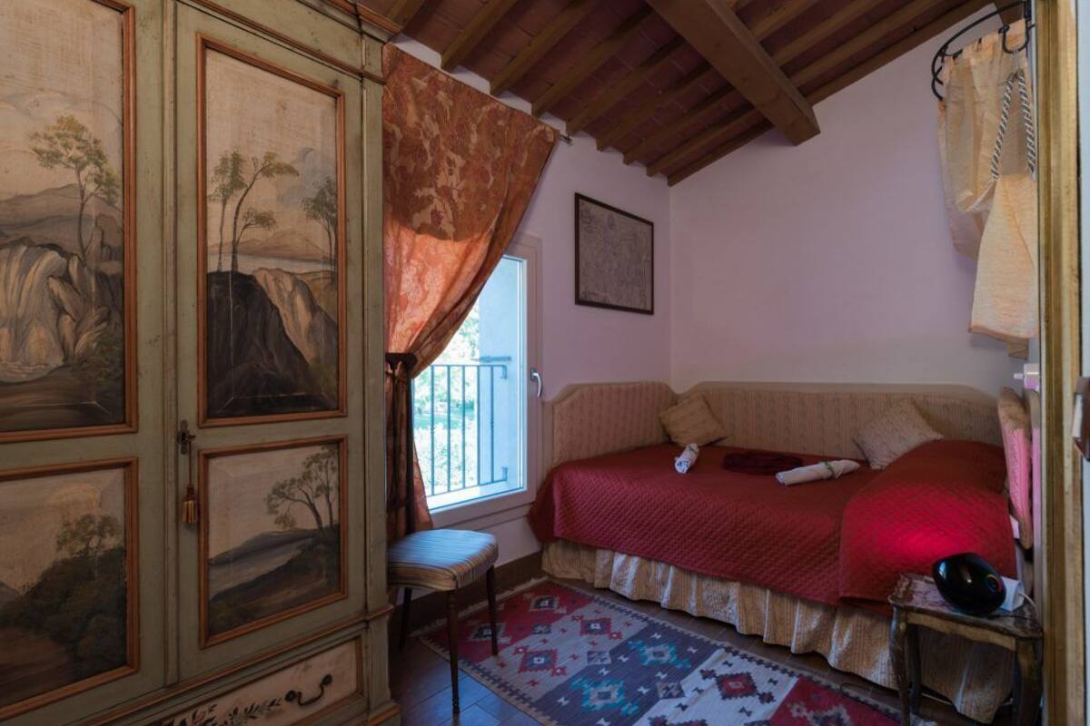 A bedroom with a bed, a chair, a cabinet with paintings, and a window.