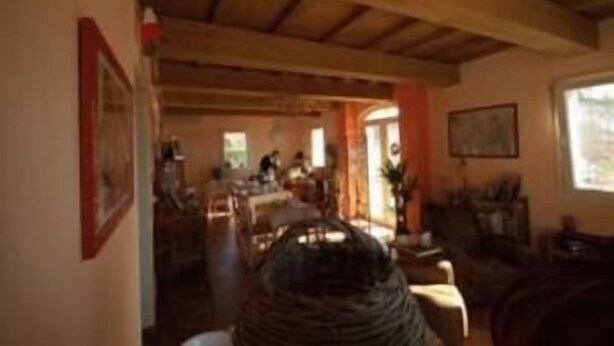 Un interior rústico con vigas de madera a la vista, una zona de comedor con mesas y sillas, y una cesta grande de fibra.
