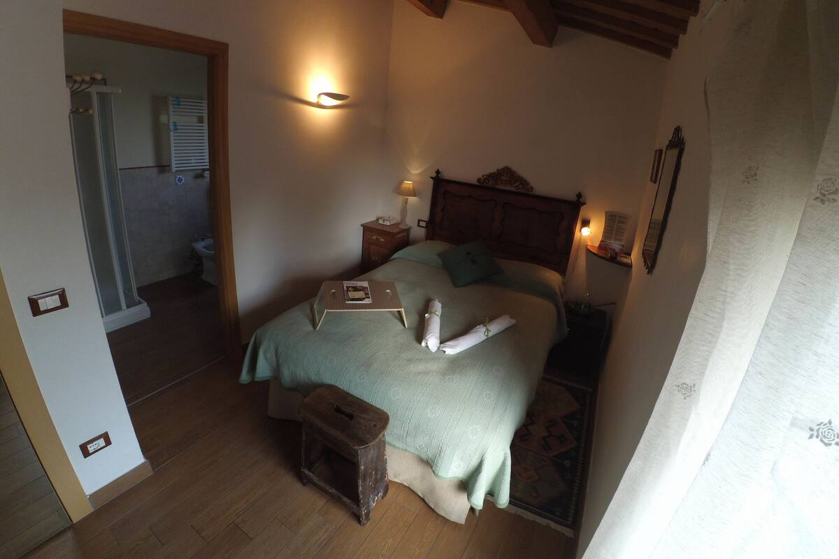 A bedroom with a bed, bedside tables, a nightstand, a wooden stool, and a mirror.