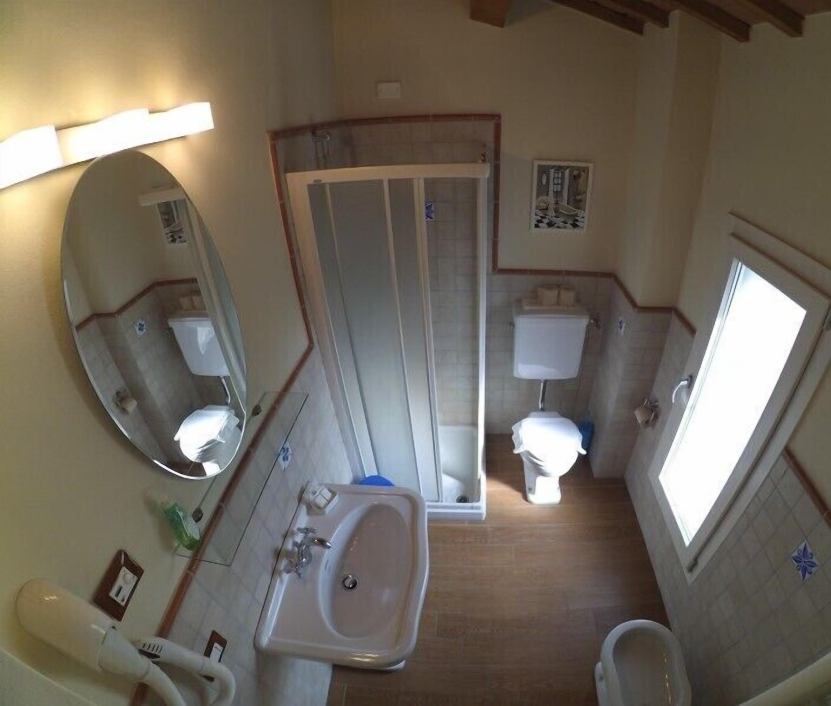 A compact bathroom with a sink, two toilets, a shower, and a mirror.