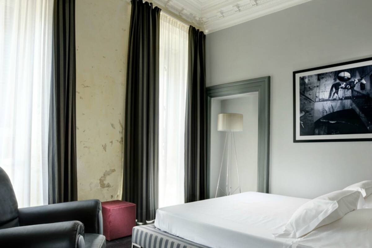 A hotel room with a bed, a chair, a lamp, and a painting on the wall.