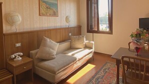 A cozy room with a sofa, a small table with a vase, a chair, a painting on the wall, and a window with a view. - Locanda da Renzo (Treviso)