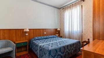 Un dormitorio con cama, una silla, una mesita de noche, una lámpara y una mesa de madera.