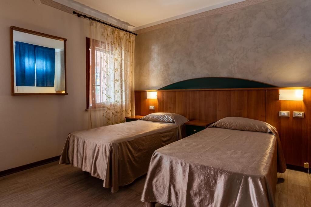 Een hotelkamer met twee enkele bedden, een grote spiegel, een raam met gordijnen en een wandlamp.