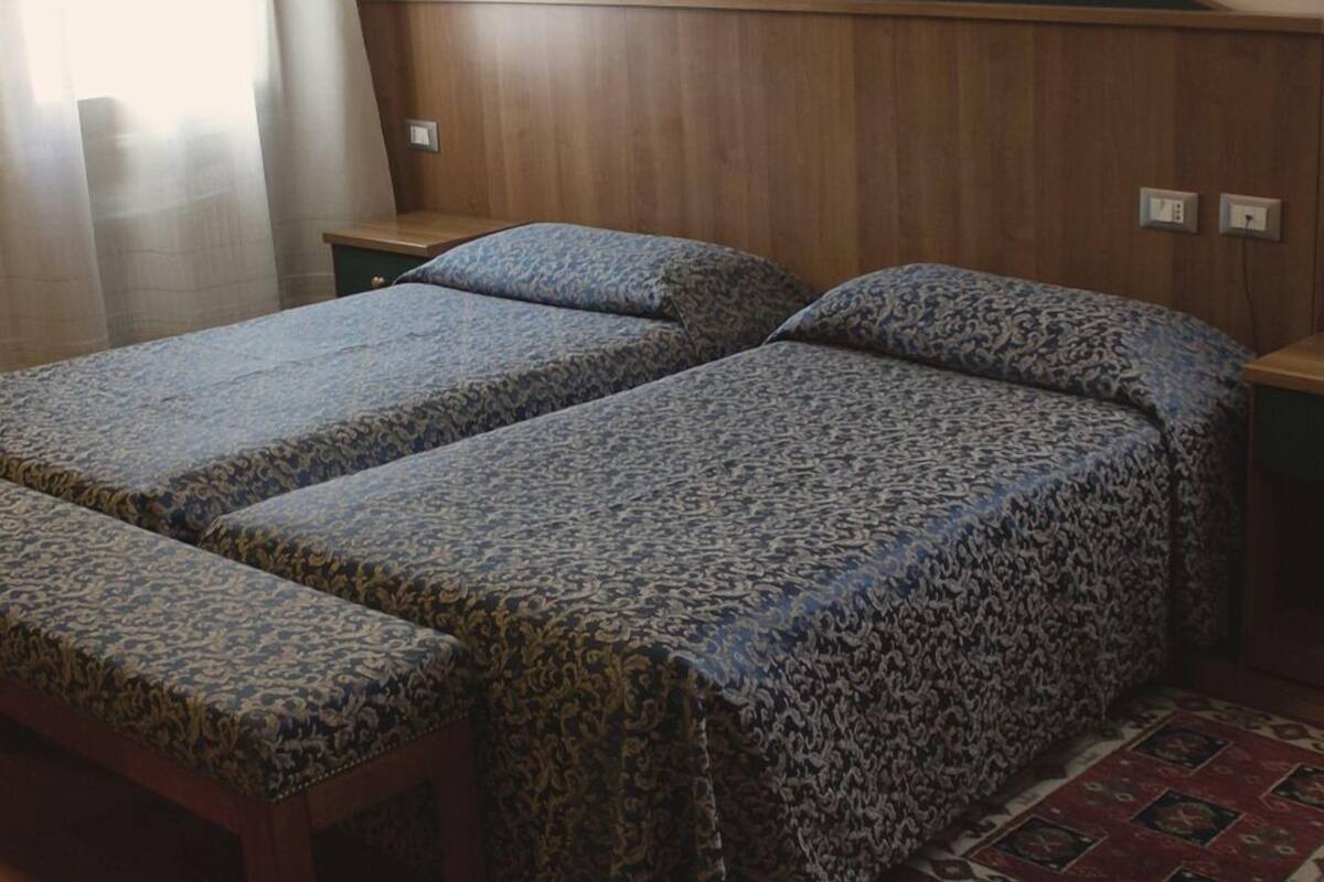 Una habitación con dos camas individuales, cabeceros de madera, una mesita de noche pequeña y una alfombra estampada.