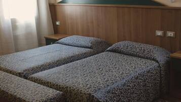 Una habitación con dos camas individuales, cabeceros de madera, una mesita de noche pequeña y una alfombra estampada.