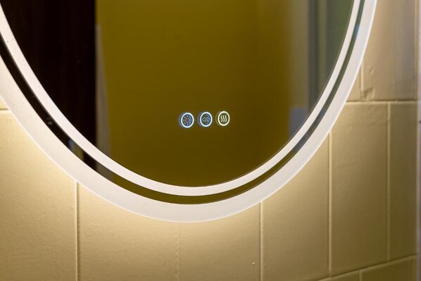 Espejo circular con marco blanco y bordes iluminados, montado en una pared con superficie texturizada.