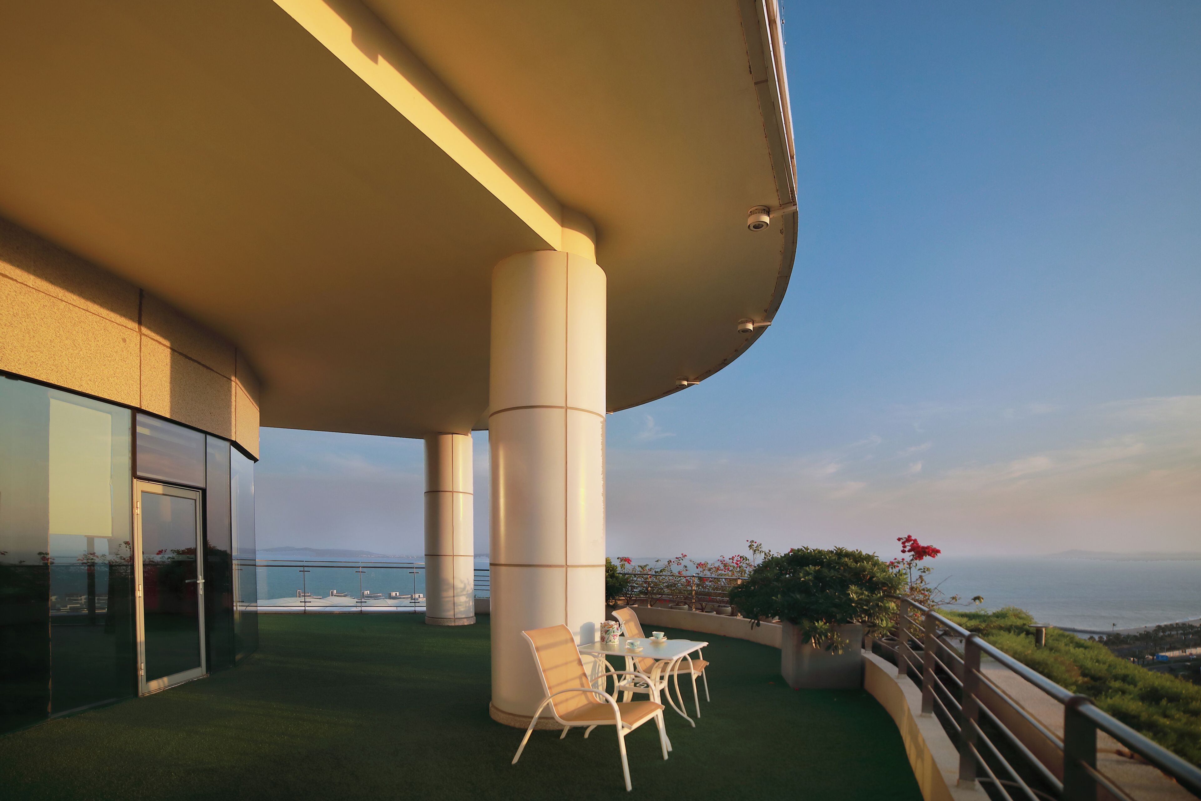 Una terraza moderna al aire libre con techo curvo, puerta de cristal y vista al mar.