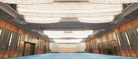 A large conference room with a blue carpet, chandeliers, and a stage with a backdrop.