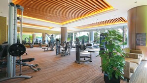 A gym with various exercise equipment, a large plant, and a seating area with a view of the outdoors. - Xiamen International Conference Center Hotel (Xiamen)