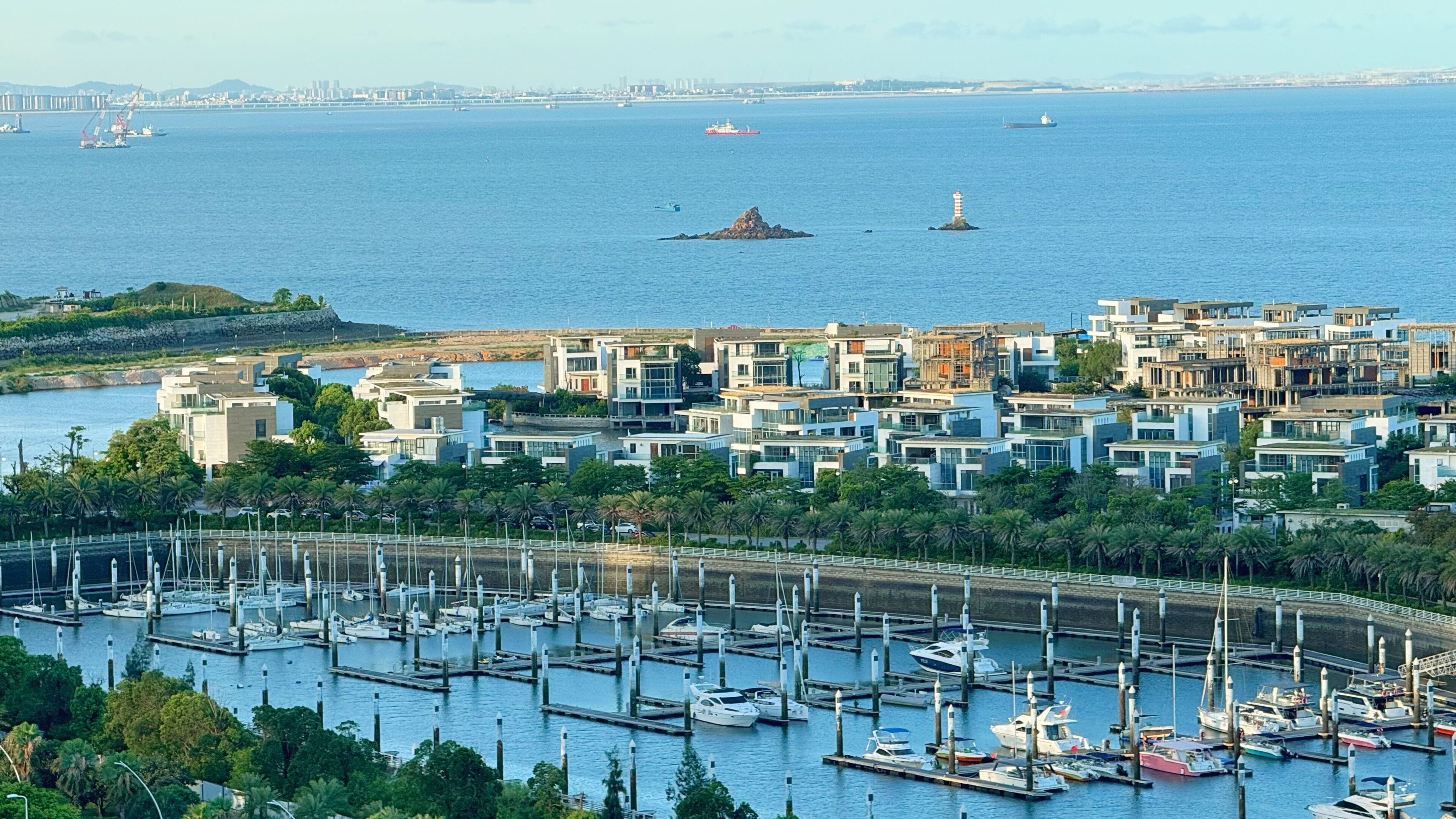A marina with multiple docks and boats, a coastal residential area with modern buildings, and a lighthouse in the distance.